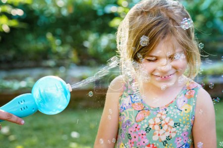 Photo for Happy little blonde preschool girl having fun with blowing soap bubble blower. Cute child playing on sunny summer day. Happy active funny healthy kid. Activity for children - Royalty Free Image