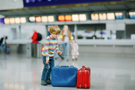Photo for Cute little kid boy with luggage, two suitcases on international airport. Mother with little girl daughter on background, Happy family wating for flight and going on vacations. Travel lifestyle - Royalty Free Image