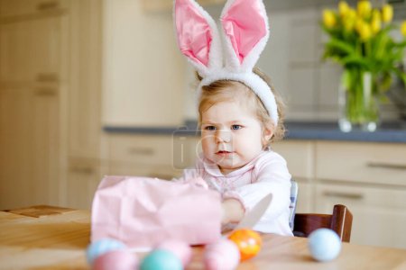 Téléchargez les photos : Petite fille mignonne tout-petit portant des oreilles de lapin de Pâques jouant avec des œufs pastel colorés. Joyeux bébé enfant déballer des cadeaux. Adorable enfant souriant sain en vêtements roses profitant de vacances en famille, - en image libre de droit