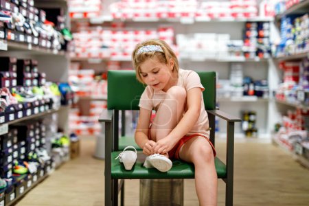 Téléchargez les photos : Happy Little Girl sélectionne et achète soigneusement de nouvelles chaussures dans un magasin, en essayant diverses options pour trouver la paire parfaite. Enfant préscolaire excité - en image libre de droit
