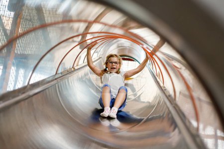 Photo for Little preschool girl riding from childrens slides on playground. Happy smiling child having fun in game center for kids - Royalty Free Image