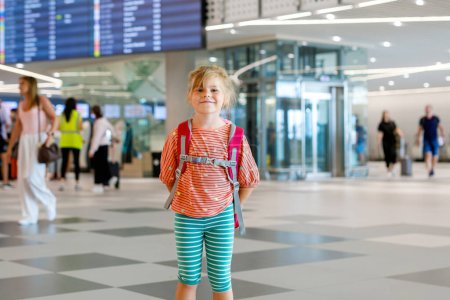 Foto de Una niña preescolar en la terminal del aeropuerto. Feliz niño que se va de vacaciones en avión. Niño sonriente con pasaporte y bolso - Imagen libre de derechos