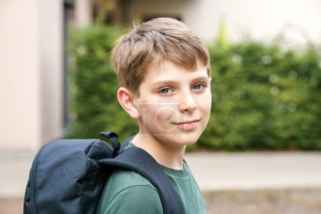 Foto de Happy preteen kid boy with backpack or satchel. Schoolkid in on the way to elementary or middle school on warm sunny summer day. Healthy child outdoors on the street in the city - Imagen libre de derechos