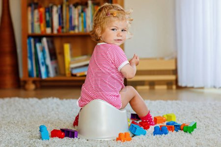Téléchargez les photos : Gros plan de mignon petit enfant de 12 mois bébé fille assis sur pot. Enfant jouant avec un jouet de poupée. Concept de formation aux toilettes. Apprentissage des bébés, étapes de développement. - en image libre de droit