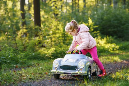 Photo for Little preschool girl driving big vintage toy car. Happy child having fun with playing outdoors. Active preschooler child enjoying warm autumn day in forest. Smiling stunning kid playing. - Royalty Free Image