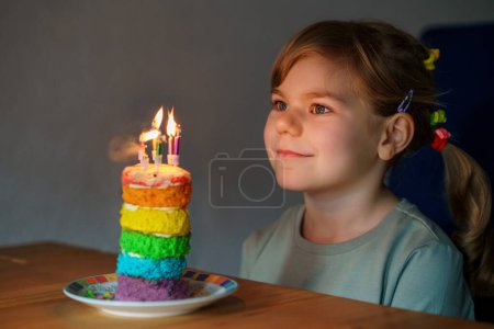 Téléchargez les photos : Happy little preschool girl celebrating birthday. Closeup of child with homemade rainbow cake, indoor. Happy healthy toddler blowing six candles on cake. Selective focus on cake. - en image libre de droit