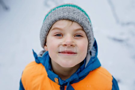 Photo for Portrait of little school kid boy in colorful clothes playing outdoors during snowfall. Active leisure with children in winter on cold snowy days. Happy healthy child having fun and playing with snow - Royalty Free Image