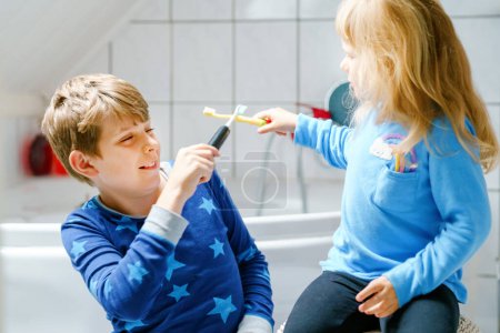 Foto de Niña preescolar y niño preadolescente cepillándose los dientes. Hermano enseñando a hermana a cepillar dientes. Felices hermanos. Dos niños divirtiéndose con la rutina dental matutina. Familia en interiores - Imagen libre de derechos