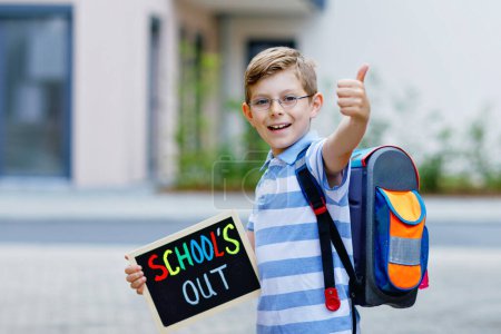 Photo for Happy little kid boy with backpack or satchel. Schoolkid on the way to school. Healthy adorable child outdoors With chalk desk for copyspace. Back to school or schools out - Royalty Free Image