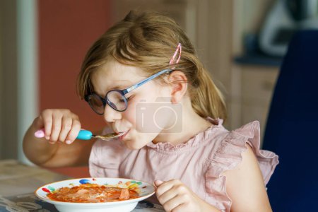 Photo for Little preschool girl eating from spoon vegetable potato soup. Healthy food for children. Happy kid at home or nursery - Royalty Free Image