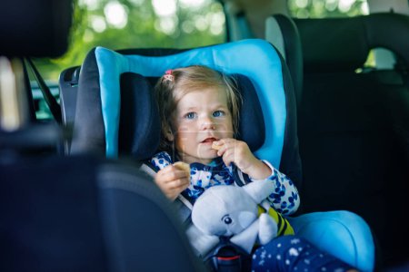 Photo for Adorable baby girl with blue eyes sitting in car safety seat. Toddler child going on family vacations and jorney. Smiling happy child during traffic jam, eating bisquit. - Royalty Free Image
