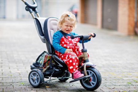 Photo for Cute adorable toddler girl sitting on pushing bicycle or tricycle. Little baby child going for a walk with parents cold cloudy day. Happy healthy kid in colorful clothes. - Royalty Free Image
