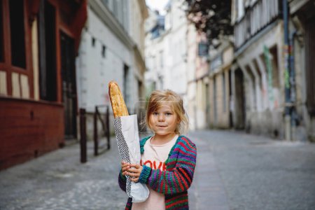 Téléchargez les photos : Adorable petite fille d'âge préscolaire avec baguette française fraîche sur le côté rue de la ville. Joyeux petit enfant à Paris, France - en image libre de droit