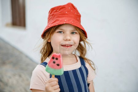 Foto de Hermosa niña come helado en el verano. Niño preescolar con helado de sandía. Niño feliz en la calle de la ciudad - Imagen libre de derechos