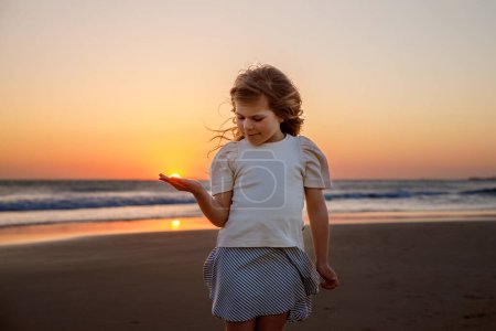 Foto de Adorable niña sonriente feliz en vacaciones de playa al atardecer. Hermoso niño preescolar lindo con pelos largos y rubios que se divierten en vacaciones familiares - Imagen libre de derechos