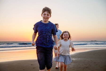 Photo for Portrait of three children, happy kids on beach at sunset. happy family, two school boys and one little preschool girl. Siblings having fun together. Bonding and family vacation. - Royalty Free Image