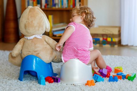 Photo for Closeup of cute little 12 months old toddler baby girl child sitting on potty. Kid playing with doll toy. Toilet training concept. Baby learning, development steps. - Royalty Free Image
