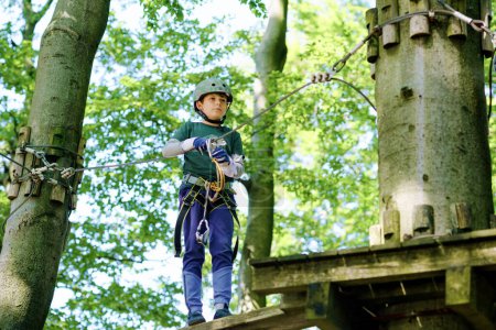 Photo for Two children in forest adventure park. Kids boys in helmet climbs on high rope trail. Agility skills and climbing outdoor amusement center for children. Outdoors activity for kid and families - Royalty Free Image