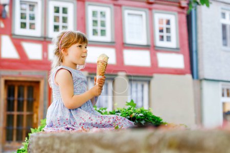 Photo for Little preschool girl eating ice cream in waffle cone on sunny summer day. Happy toddler child eat icecream dessert. Sweet food on hot warm summertime days. Bright light, colorful ice-cream. - Royalty Free Image