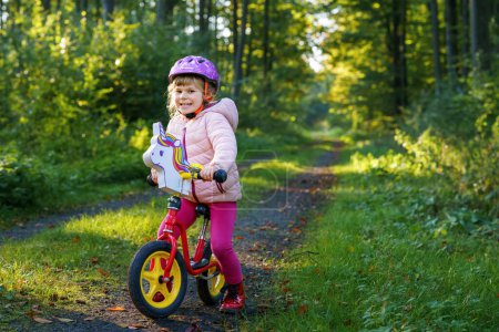 Photo for Child riding balance bike. Kids on bicycle in sunny forest. Little girl enjoying to ride glider bike on warm day. Preschooler learning to balance on run bicycle in safe helmet. Sport activity. - Royalty Free Image