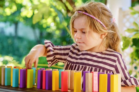 Photo for Little preschool girl playing board game with colorful bricks domino. Happy child build tower of wooden blocks, developing fine motor skills, home joint games. Leisure activities for children at home - Royalty Free Image