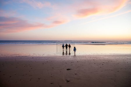 Photo for Portrait silhouettes of three children and mum happy kids with mother on beach at sunset. happy family, woman, two school boys and one little preschool girl. Siblings having fun together. Bonding. - Royalty Free Image