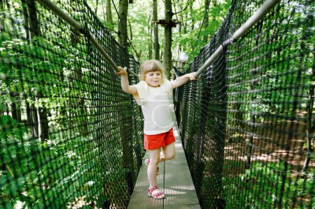 Photo for Cute little preschool girl walking on high tree-canopy trail with wooden walkway and ropeways on Hoherodskopf in Germany. Happy active child exploring treetop path. Funny activity for family outdoors. - Royalty Free Image