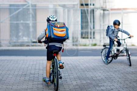 Photo for Two school kid boys in safety helmet riding with bike in the city with backpacks. Happy children in colorful clothes biking on bicycles on way to school. Safe way for kids outdoors to school. - Royalty Free Image