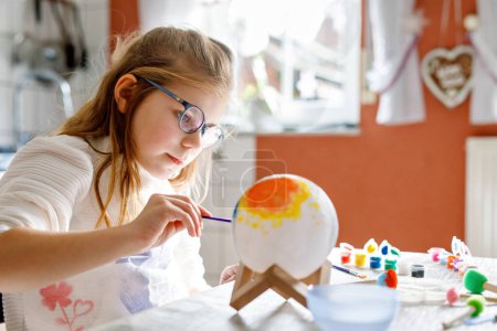 Foto de Niña pintando globo o bola con colores. Niño de la escuela haciendo globo terráqueo para proyecto escolar. Niño feliz con anteojos sosteniendo cepillo - Imagen libre de derechos