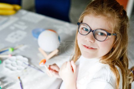 Photo for Little girl painting globe or ball with colors. School child making earth globe for school project. Happy kid with eyeglasses holding brush - Royalty Free Image