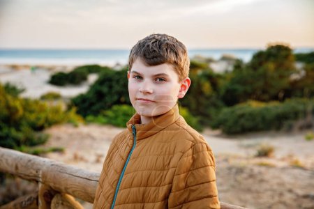 Photo for Happy cheerful teenager standing on beach at sunset. happy preteen handsome boy smiling at the camera. Kid on family vacation at the sea - Royalty Free Image