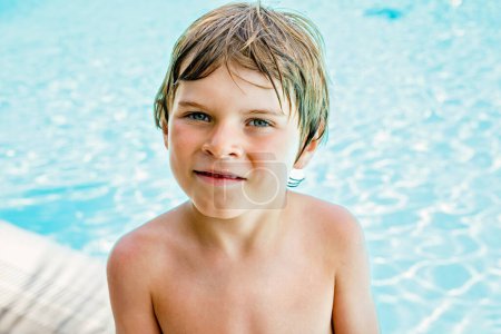 Foto de Retrato de un niño feliz descansando cerca de la piscina y divirtiéndose en vacaciones familiares en un complejo hotelero. Niños sanos jugando en el agua, nadando y salpicando - Imagen libre de derechos
