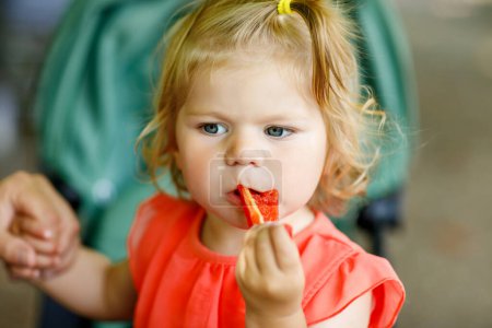 Foto de Pequeña niña comiendo pimiento rojo y verduras para un almuerzo saludable sentada en un cochecito de bebé. niño feliz y comida saludable. - Imagen libre de derechos