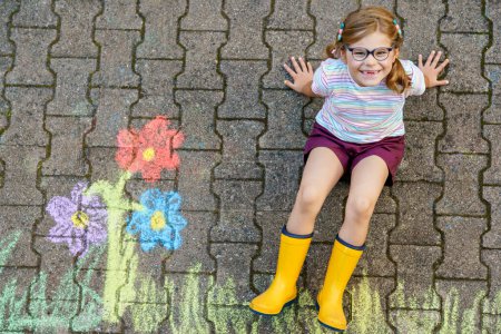 Photo for Cute little girl and flowers painted with colorful chalks on asphalt. Happy preschool child having fun with painting chalk picture. Creative leisure for children, drawing and painting - Royalty Free Image
