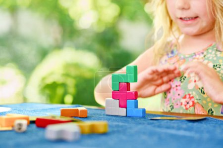 Téléchargez les photos : Little preschool girl playing board game with colorful bricks. Happy child build tower of wooden blocks, developing fine motor skills, home joint games. Leisure activities for children at home - en image libre de droit