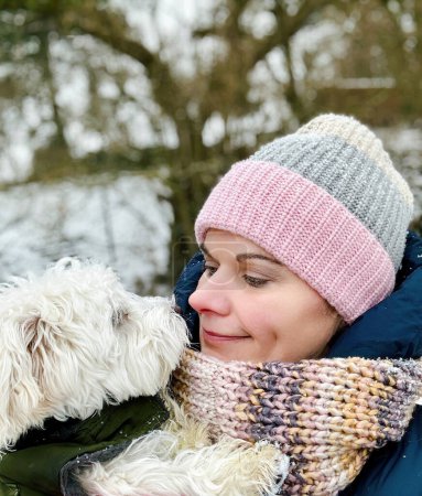 Foto de Retrato de una mujer en ropa de invierno con su perro cachorro. Mujer feliz y pequeña mascota maltesa juntos - Imagen libre de derechos