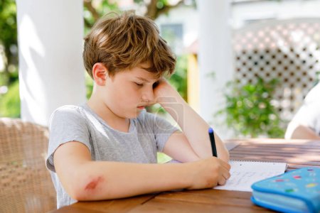Fleißiger trauriger Schuljunge, der während der Quarantäne-Zeit Hausaufgaben wegen der Coronapandemie macht. Verärgertes müdes Kind bei Einschulung zu Hause in Coronavirus-Zeit, Schulen geschlossen