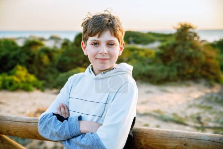 Photo for Happy cheerful teenager standing on beach at sunset. happy preteen boy smiling at the camera. Kid on family vacation at the sea - Royalty Free Image