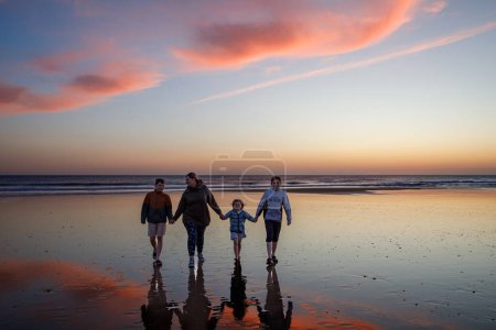 Téléchargez les photos : Portrait silhouettes de trois enfants et maman enfants heureux avec mère sur la plage au coucher du soleil. famille heureuse, femme, deux écoliers et une petite fille d'âge préscolaire. Des frères et sœurs qui s'amusent ensemble. Liaison. - en image libre de droit