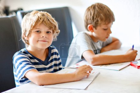 Téléchargez les photos : Deux garçons qui font leurs devoirs ensemble. Frères, frères et sœurs et jumeaux apprenant à la maison. Élèves du primaire, enfants écrivant - en image libre de droit
