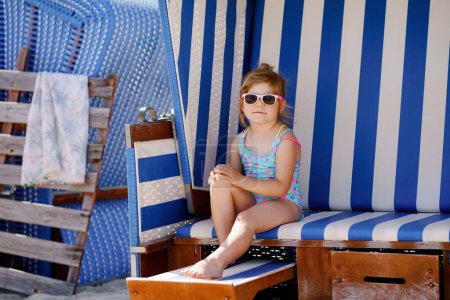 Little preschool girl resting on beach chair. Cute happy toddler child on family vacations on the sea. Kid playing, having outdoors fun on roofed wicker beach basket on German Baltic Sea coastline