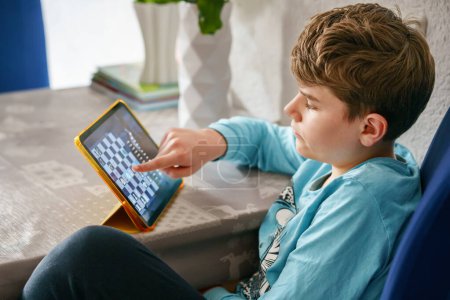 Foto de Adolescente caucásico jugando al ajedrez en la tableta. Niño niño juega juego con oponente virtual - Imagen libre de derechos