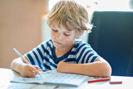 Portrait de garçon fatigué bouleversé faisant ses devoirs dans la cuisine à la maison. École élémentaire studing écriture et apprentissage. Enfant triste et en colère