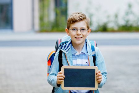 Happy little kid boy with backpack or satchel and glasses. Schoolkid on the way to school. Healthy adorable child outdoors On desk Last day third grade in German. Schools out.