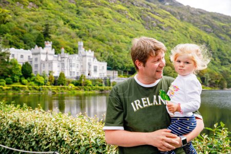 father with little daughter with Kylemore Abbey on background. Man and toddler girl. Family and small children vacations in Ireland.