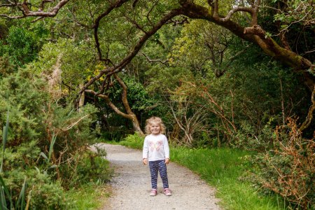 Foto de Linda niñita feliz corriendo por el sendero de la naturaleza en el parque nacional Connemara en Irlanda. Niño sonriente y riente que se divierte pasando vacaciones familiares en la naturaleza. Viajar con niños pequeños. - Imagen libre de derechos