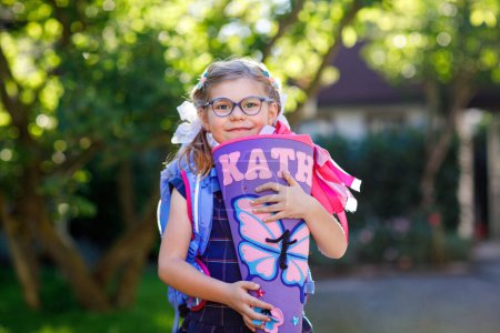 Photo for Happy little kid girl with eye glasses with backpack or satchel and big school bag or gift cone traditional in Germany for the first day of school. Healthy adorable child outdoors. Back to school. - Royalty Free Image