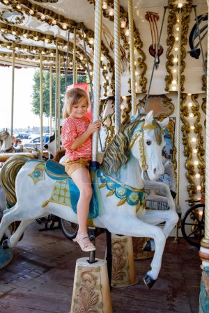 Fröhliches, positives Vorschulmädchen bei einer Fahrt auf dem alten Jahrgangs-Karussell in der Stadt St. Malo France. Lächelndes Kind auf einem Pferd