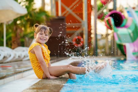 Photo for Little preschool girl playing in outdoor swimming pool by sunset. Child learning to swim in outdoor pool, splashing with water, laughing having fun. Family vacations. Healthy children sport activity. - Royalty Free Image