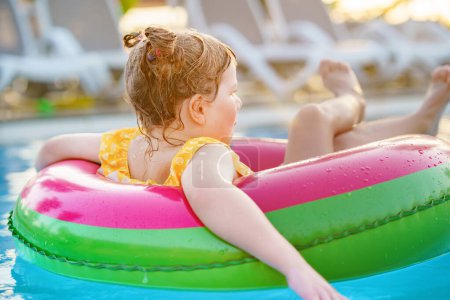 Photo for Happy little girl with inflatable toy ring float in swimming pool. Little preschool child learning to swim and dive in outdoor pool of hotel resort. Healthy sport activity and fun for children - Royalty Free Image
